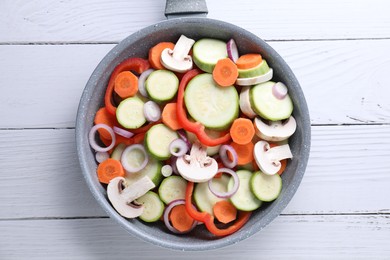 Photo of Frying pan with mix of fresh vegetables and mushrooms on white wooden table, top view