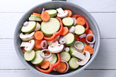 Photo of Frying pan with mix of fresh vegetables and mushrooms on white wooden table, top view