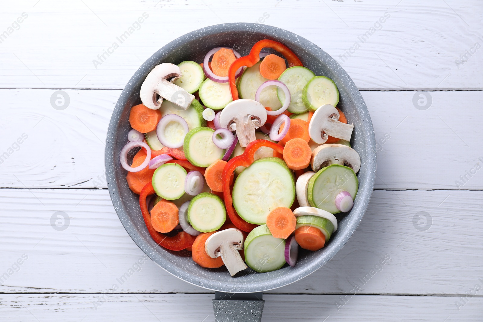 Photo of Frying pan with mix of fresh vegetables and mushrooms on white wooden table, top view