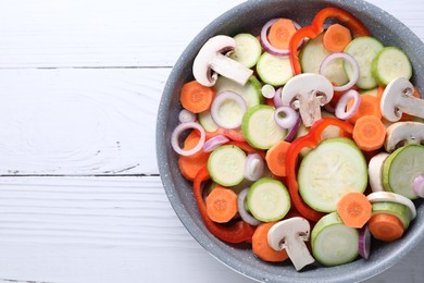 Photo of Frying pan with mix of fresh vegetables and mushrooms on white wooden table, top view. Space for text