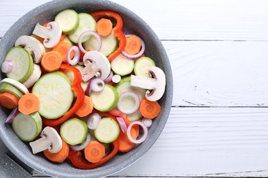 Photo of Frying pan with mix of fresh vegetables and mushrooms on white wooden table, top view. Space for text