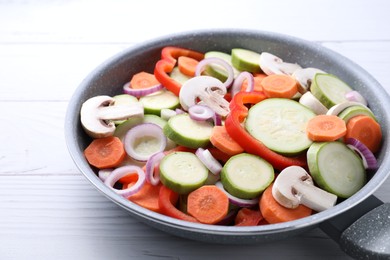 Photo of Frying pan with mix of fresh vegetables and mushrooms on white wooden table, closeup