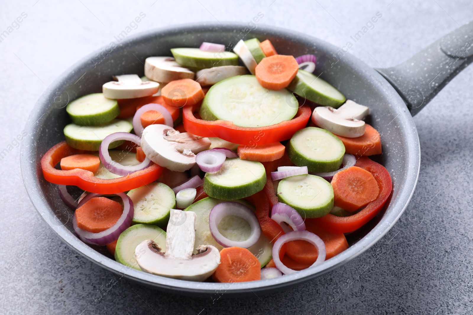 Photo of Frying pan with mix of fresh vegetables and mushrooms on grey table, closeup