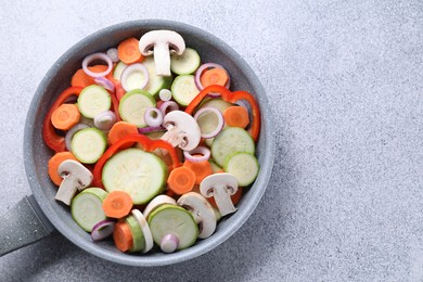 Photo of Frying pan with mix of fresh vegetables and mushrooms on grey table, top view. Space for text