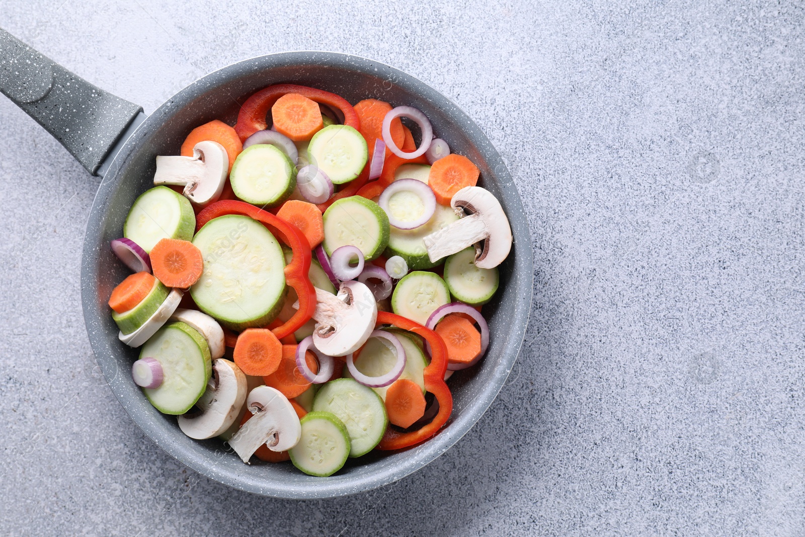 Photo of Frying pan with mix of fresh vegetables and mushrooms on grey table, top view. Space for text