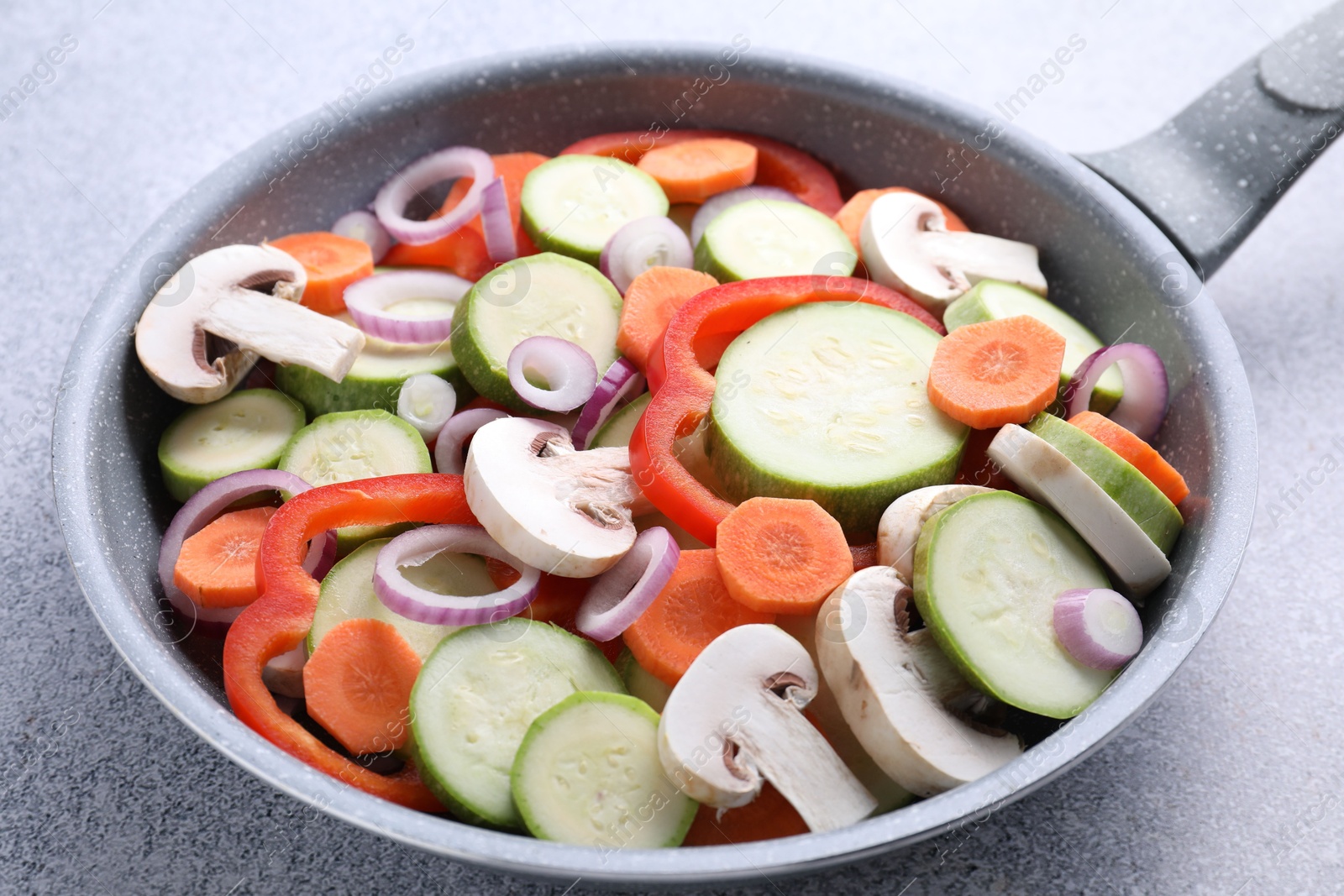 Photo of Frying pan with mix of fresh vegetables and mushrooms on grey table, closeup