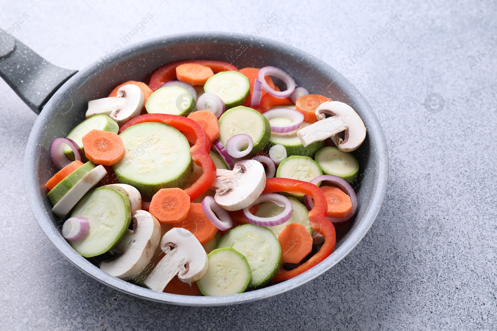 Photo of Frying pan with mix of fresh vegetables and mushrooms on grey table, closeup