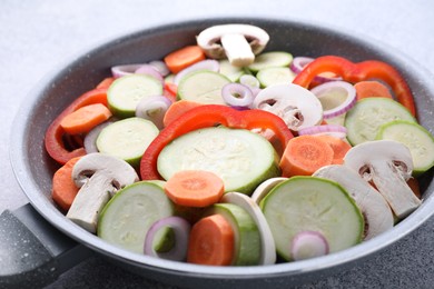 Photo of Frying pan with mix of fresh vegetables and mushrooms on grey table, closeup