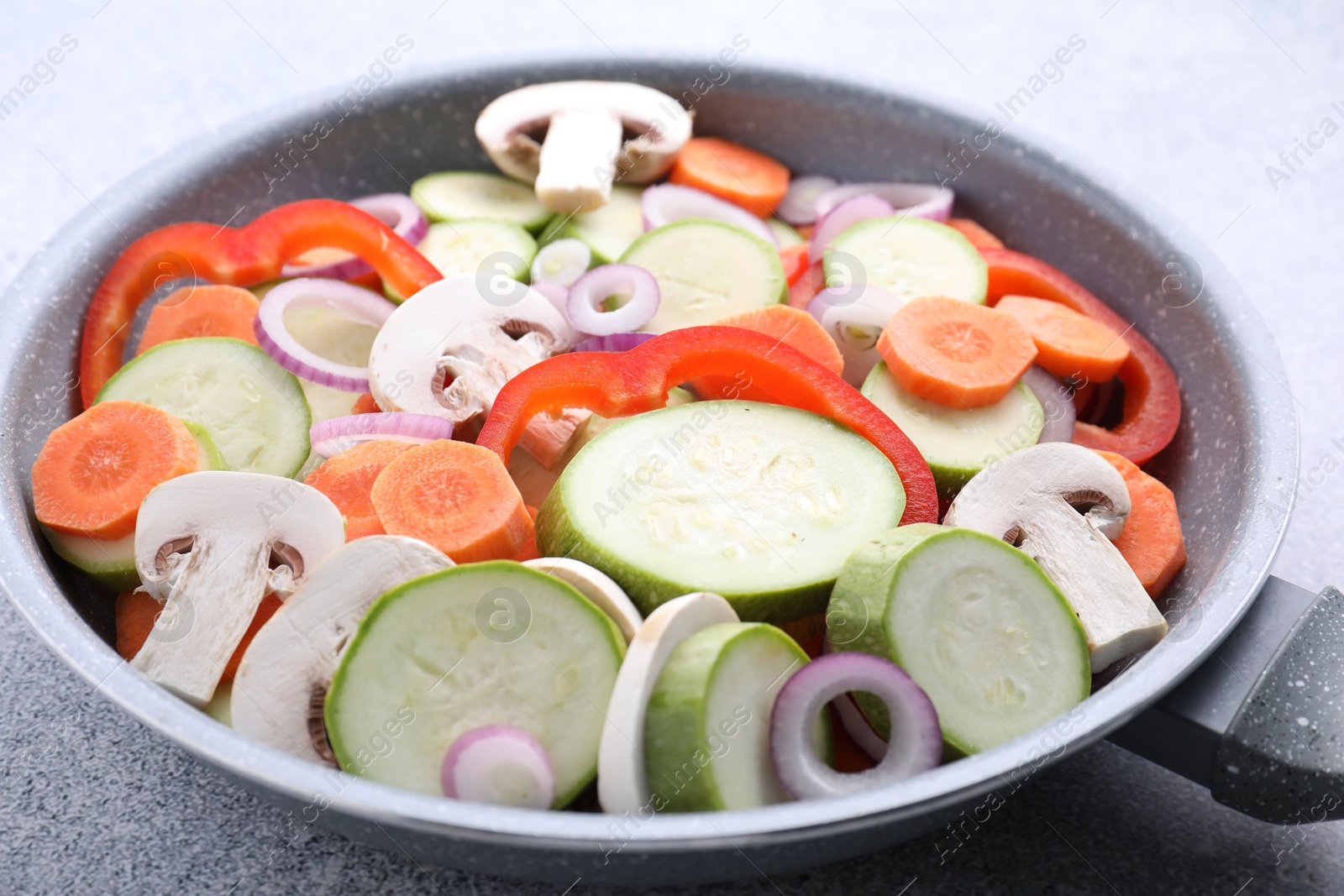 Photo of Frying pan with mix of fresh vegetables and mushrooms on grey table, closeup