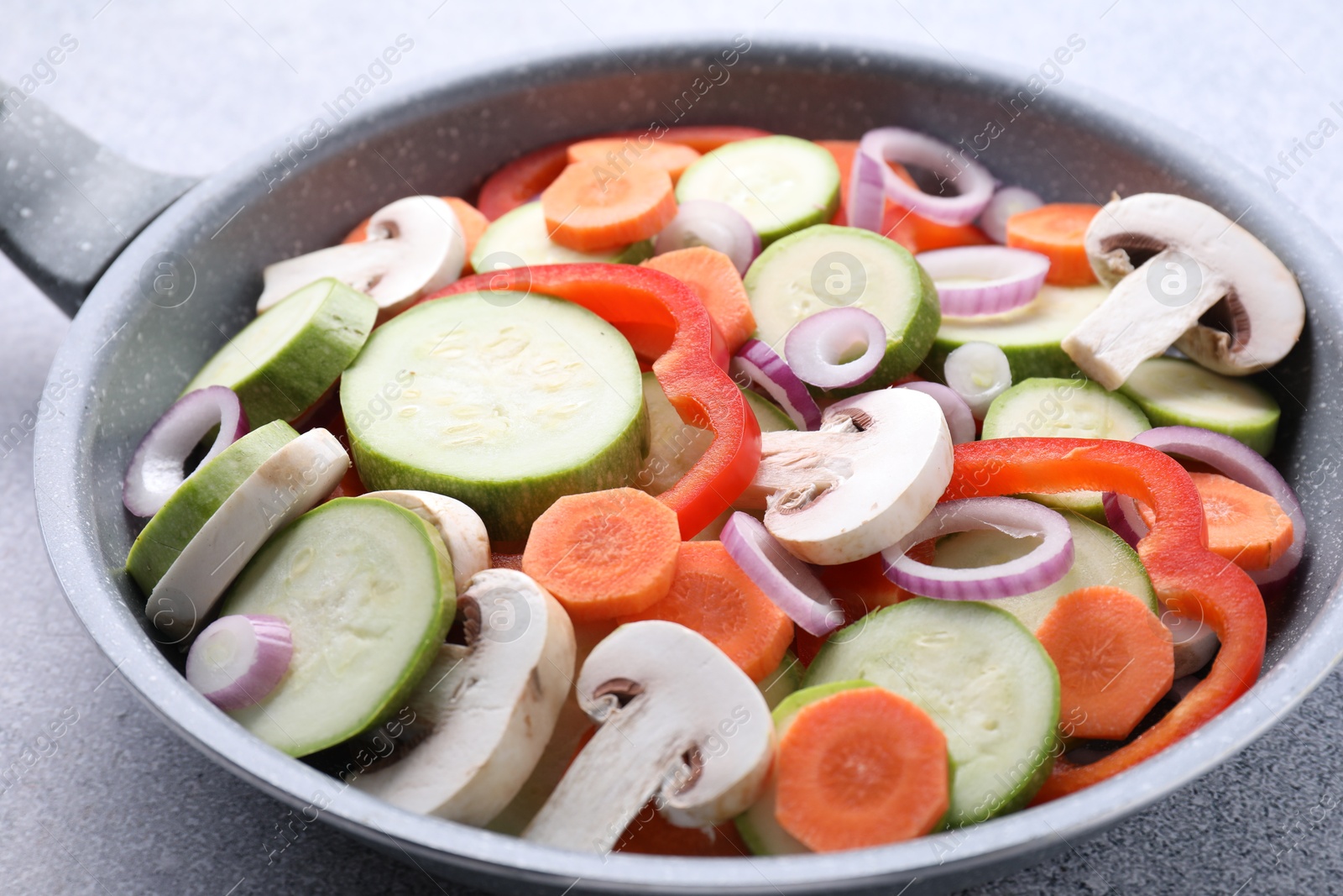 Photo of Frying pan with mix of fresh vegetables and mushrooms on grey table, closeup