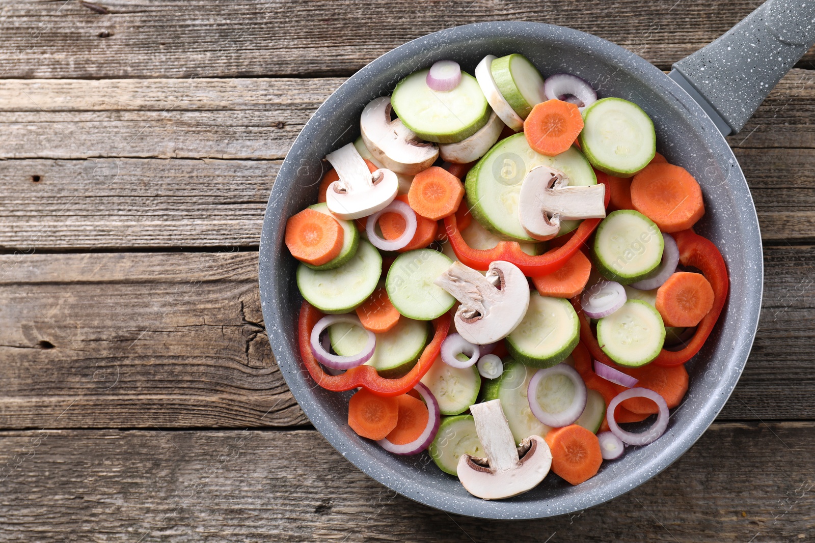 Photo of Frying pan with mix of fresh vegetables and mushrooms on wooden table, top view