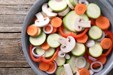 Photo of Frying pan with mix of fresh vegetables and mushrooms on wooden table, top view