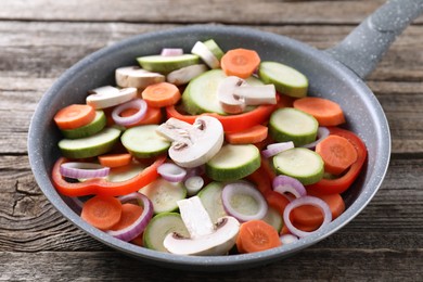 Photo of Frying pan with mix of fresh vegetables and mushrooms on wooden table, closeup