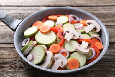 Photo of Frying pan with mix of fresh vegetables and mushrooms on wooden table, closeup