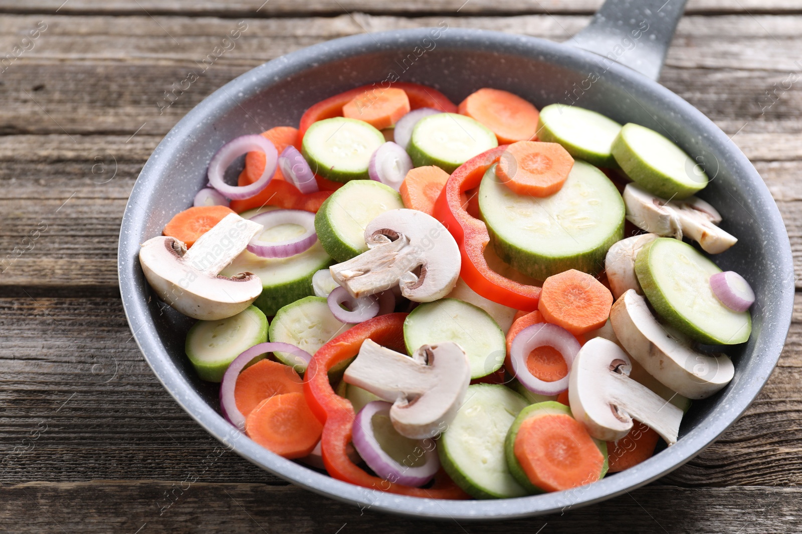 Photo of Frying pan with mix of fresh vegetables and mushrooms on wooden table, closeup