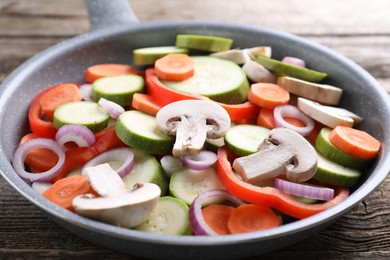 Photo of Frying pan with mix of fresh vegetables and mushrooms on wooden table, closeup