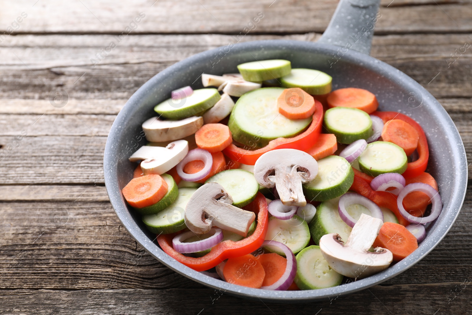 Photo of Frying pan with mix of fresh vegetables and mushrooms on wooden table, closeup