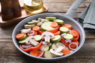 Photo of Frying pan with mix of fresh vegetables and mushrooms on wooden table, closeup