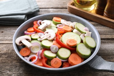 Photo of Frying pan with mix of fresh vegetables and mushrooms on wooden table, closeup