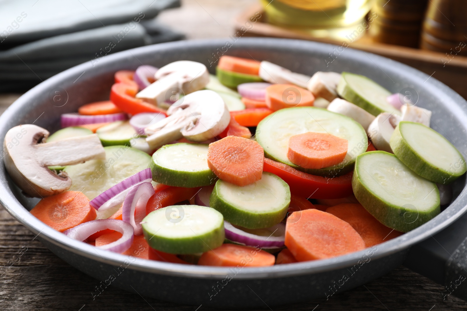 Photo of Frying pan with mix of fresh vegetables and mushrooms on wooden table, closeup