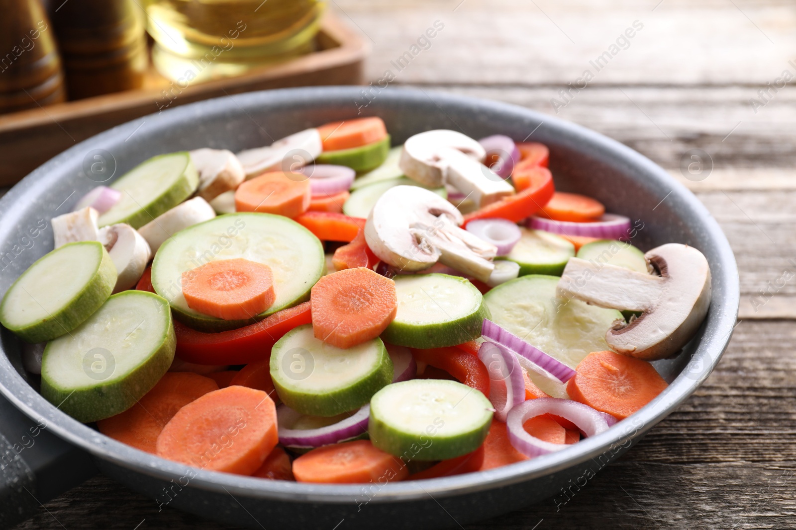 Photo of Frying pan with mix of fresh vegetables and mushrooms on wooden table, closeup