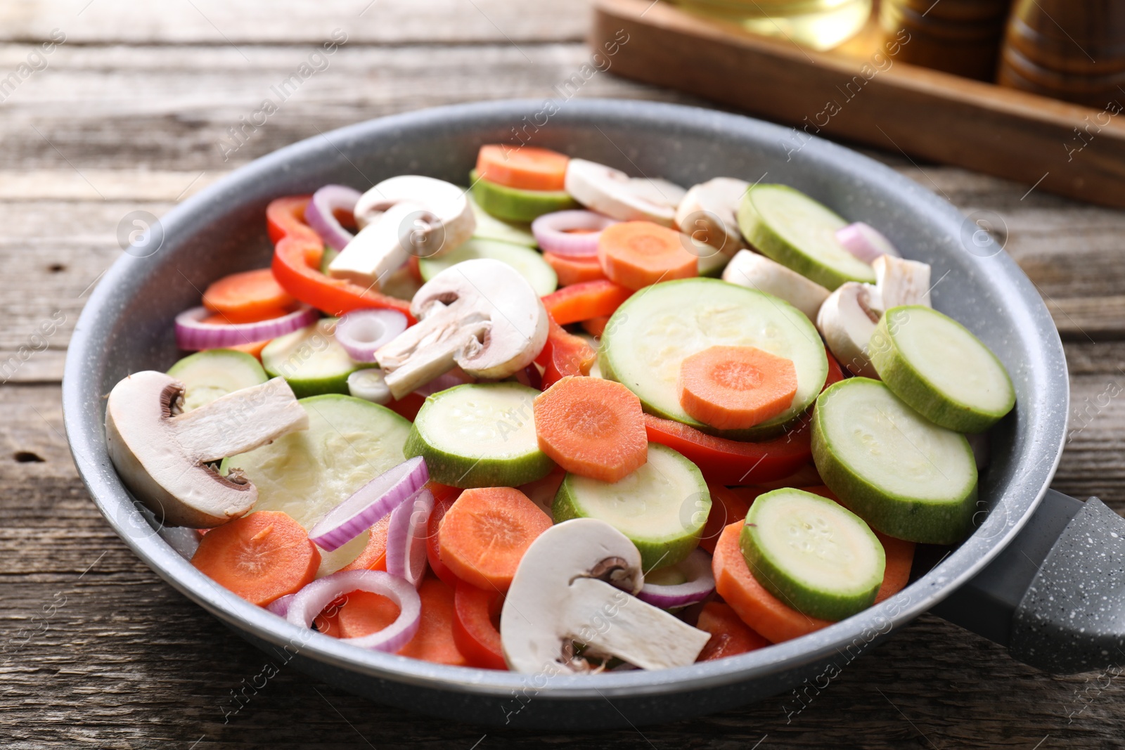 Photo of Frying pan with mix of fresh vegetables and mushrooms on wooden table, closeup