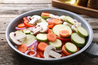 Photo of Frying pan with mix of fresh vegetables and mushrooms on wooden table, closeup