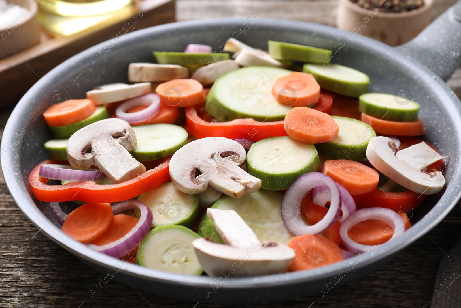 Photo of Frying pan with mix of fresh vegetables and mushrooms on wooden table, closeup