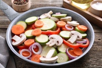 Photo of Frying pan with mix of fresh vegetables and mushrooms on wooden table, closeup