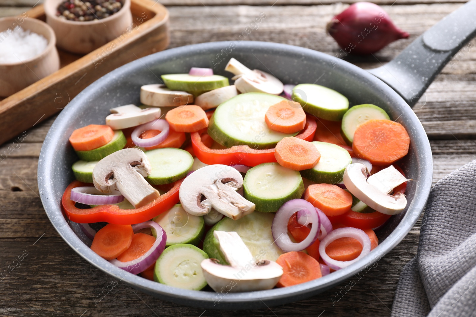 Photo of Frying pan with mix of fresh vegetables and mushrooms on wooden table, closeup