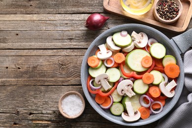 Frying pan with mix of fresh vegetables, mushrooms and spices on wooden table, flat lay. Space for text