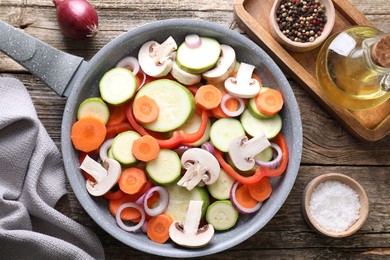 Photo of Frying pan with mix of fresh vegetables, mushrooms and spices on wooden table, flat lay