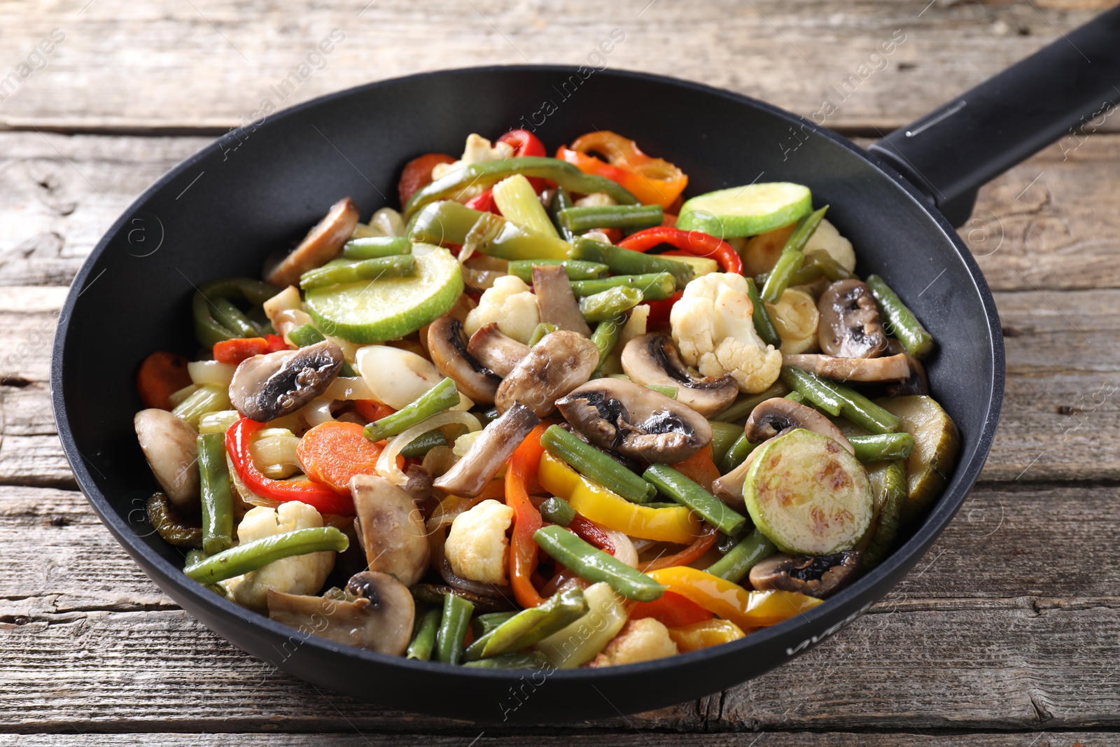 Photo of Different vegetables and mushrooms in frying pan on wooden table, closeup