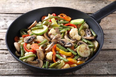 Photo of Different vegetables and mushrooms in frying pan on wooden table, closeup