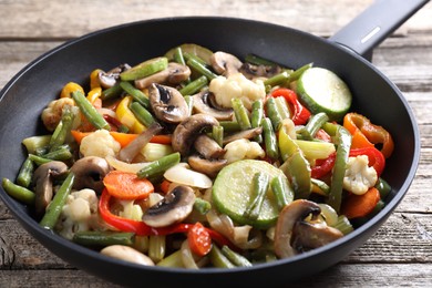 Photo of Different vegetables and mushrooms in frying pan on wooden table, closeup