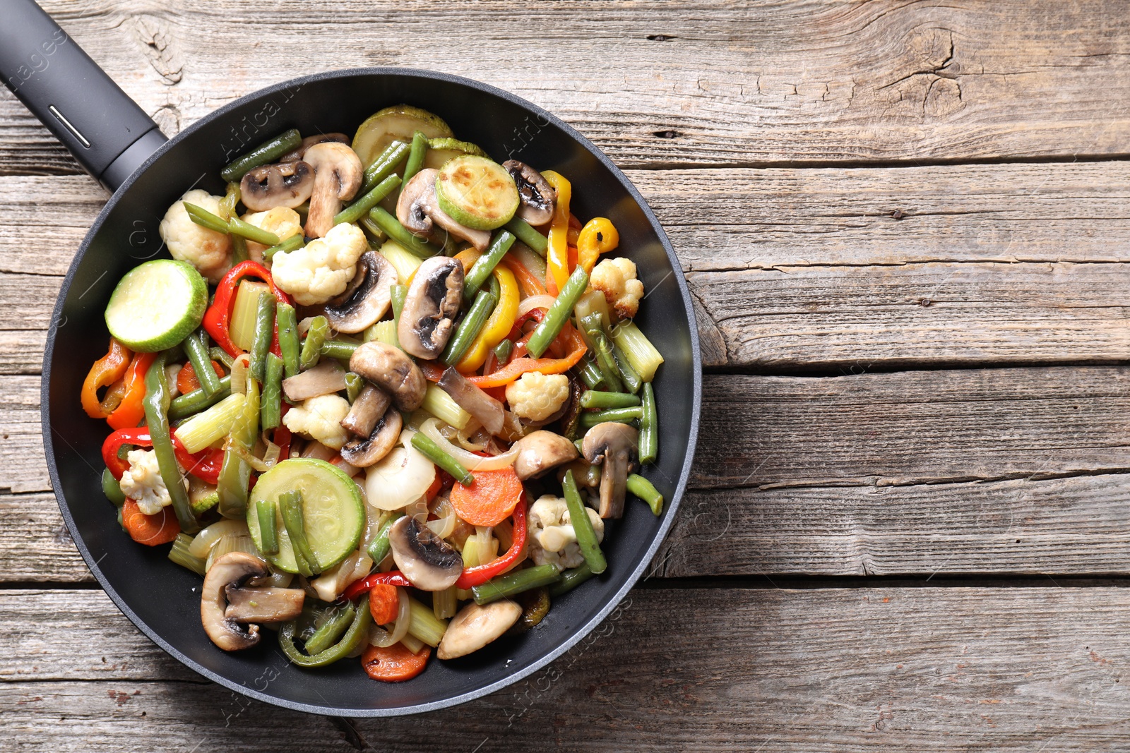 Photo of Different vegetables and mushrooms in frying pan on wooden table, top view. Space for text