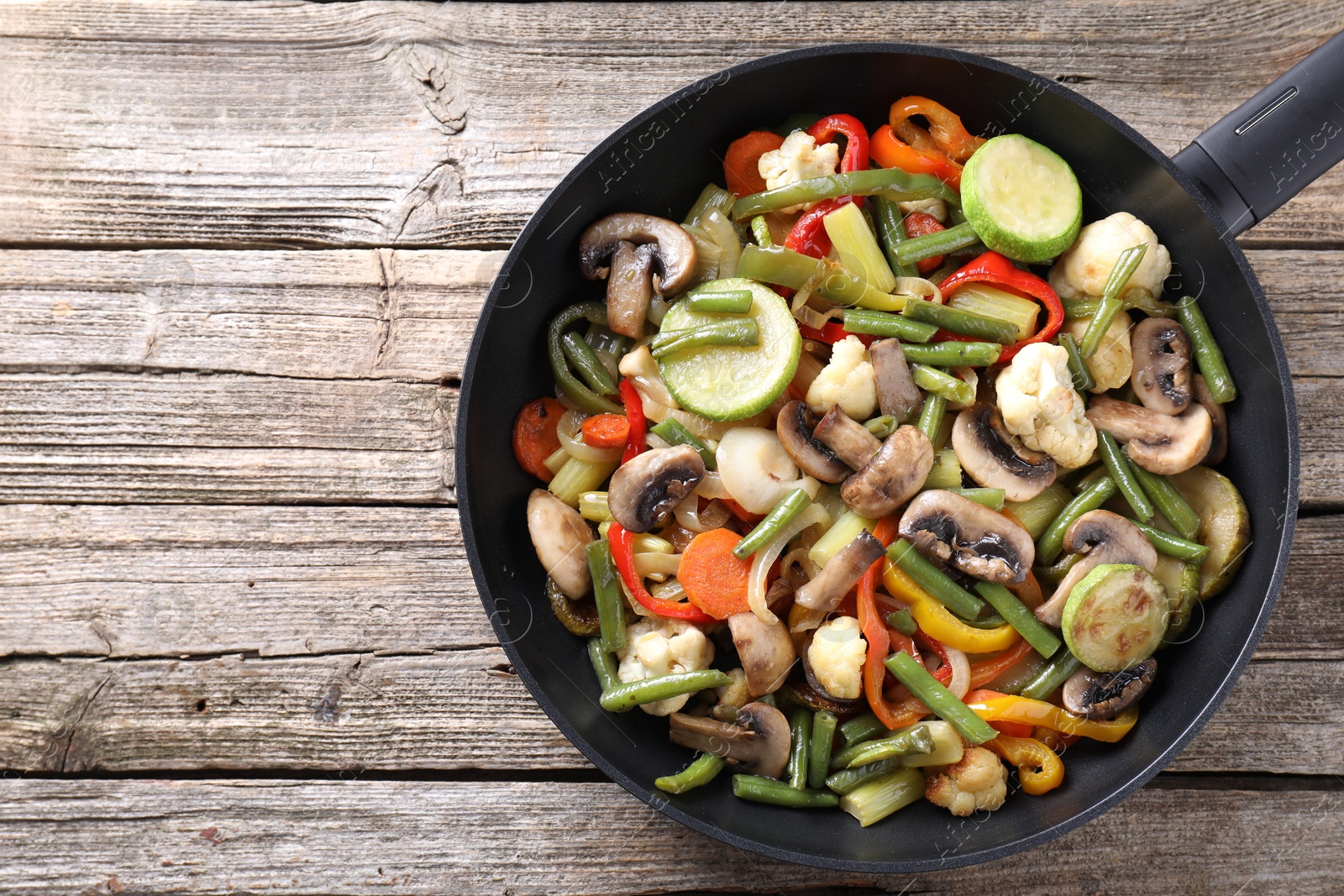 Photo of Different vegetables and mushrooms in frying pan on wooden table, top view. Space for text