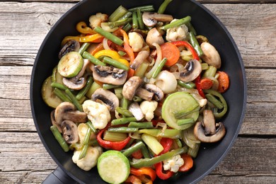 Photo of Different vegetables and mushrooms in frying pan on wooden table, top view