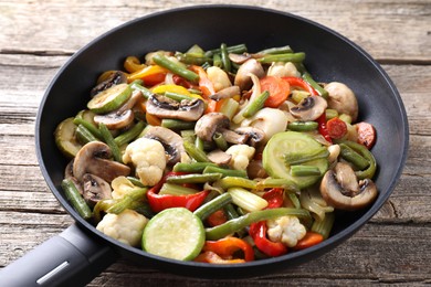 Photo of Different vegetables and mushrooms in frying pan on wooden table, closeup