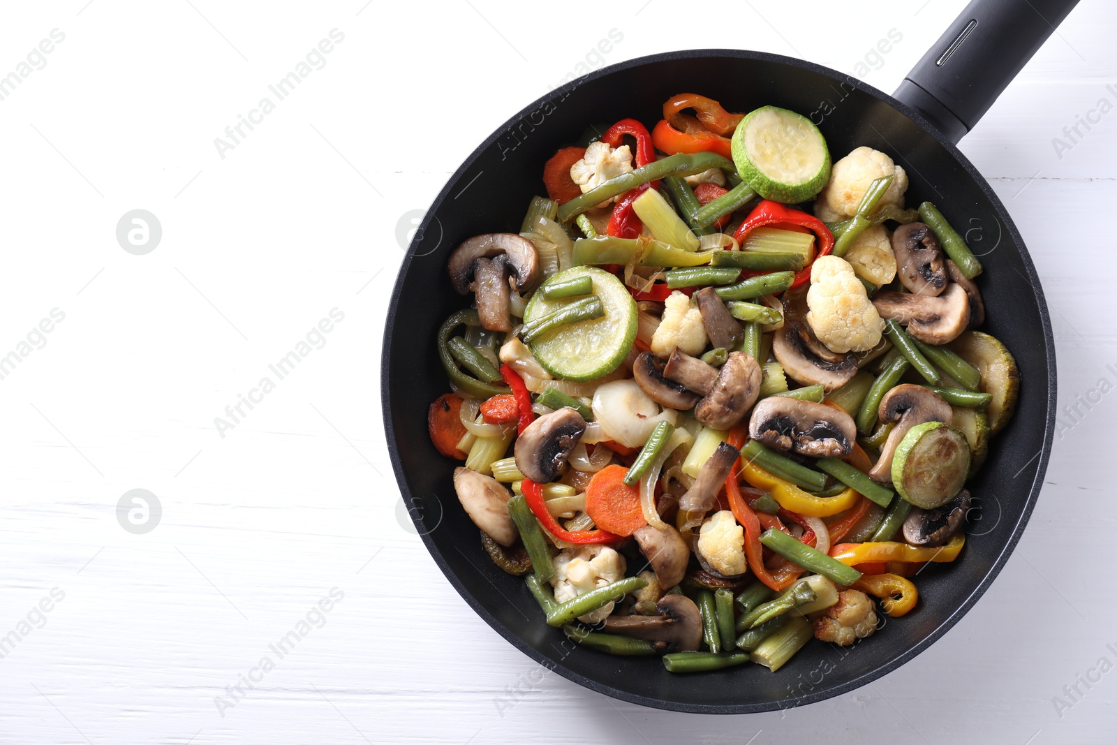 Photo of Different vegetables and mushrooms in frying pan on white table, top view. Space for text