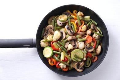 Photo of Different vegetables and mushrooms in frying pan on white table, top view