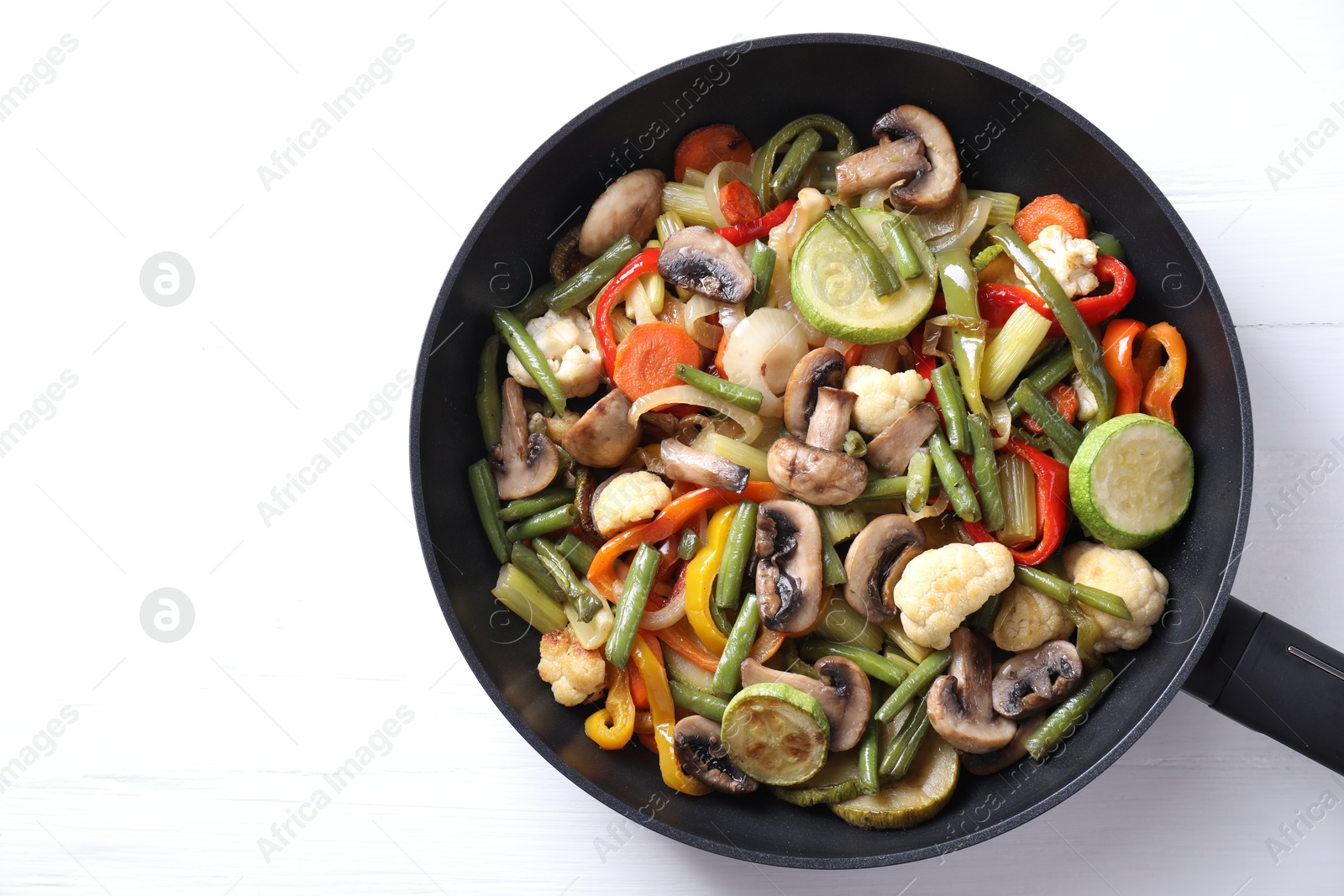 Photo of Different vegetables and mushrooms in frying pan on white table, top view. Space for text