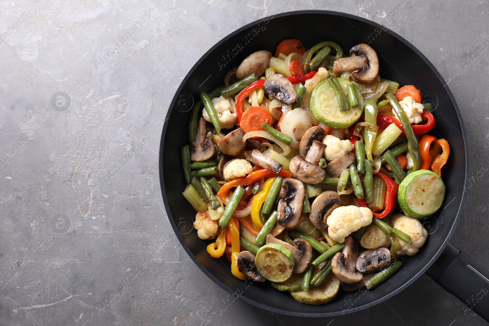 Photo of Different vegetables and mushrooms in frying pan on grey table, top view. Space for text