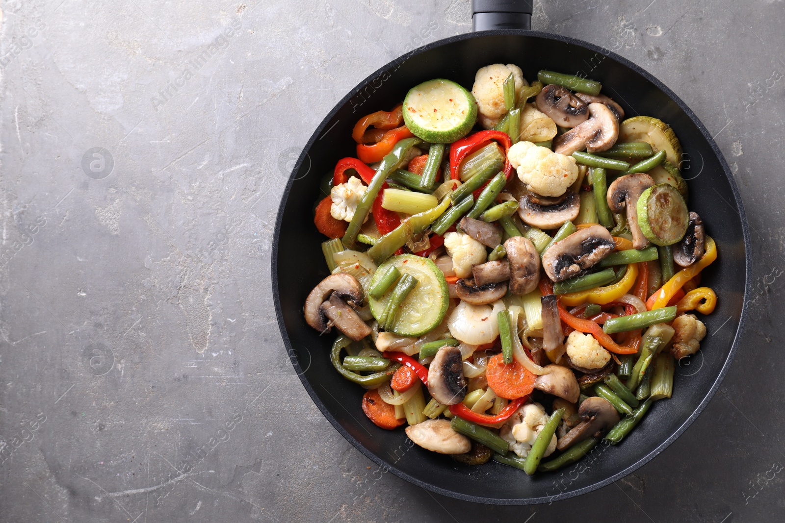 Photo of Different vegetables and mushrooms in frying pan on grey table, top view. Space for text