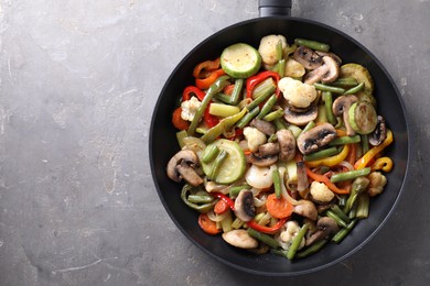 Photo of Different vegetables and mushrooms in frying pan on grey table, top view. Space for text