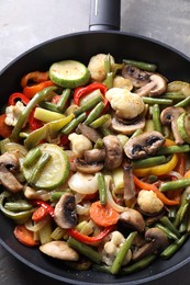 Photo of Different vegetables and mushrooms in frying pan on grey table, top view