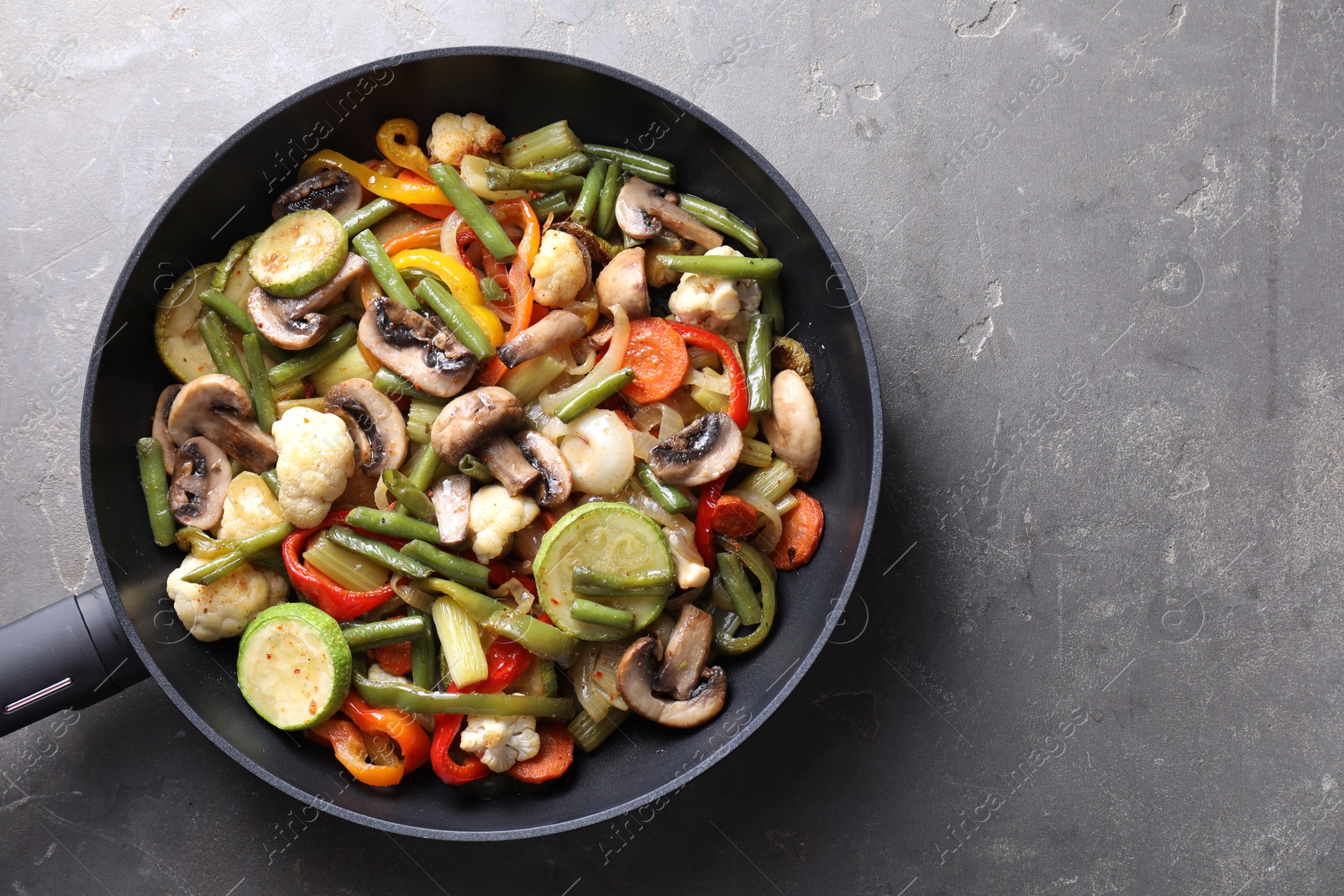 Photo of Different vegetables and mushrooms in frying pan on grey table, top view. Space for text