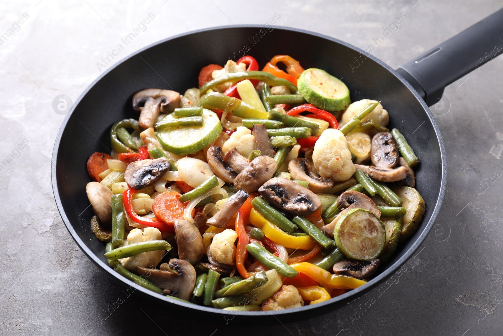 Photo of Different vegetables and mushrooms in frying pan on grey table, closeup