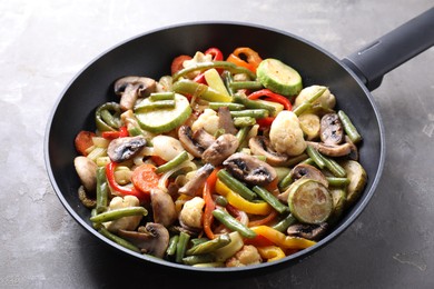 Different vegetables and mushrooms in frying pan on grey table, closeup