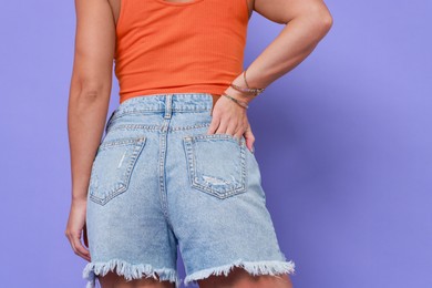 Photo of Woman wearing stylish denim shorts on violet background, closeup. Space for text